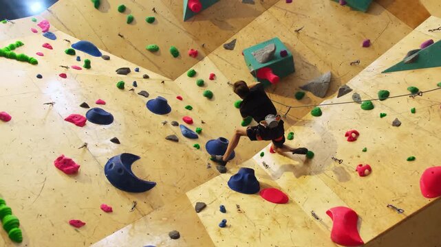 Young climber ascends wall by deftly clinging to ledges. Safety rope helps sportsman feel safe in case of fall from height