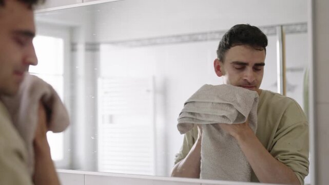 A man dries his face with a towel after washing his face, part of his daily routine