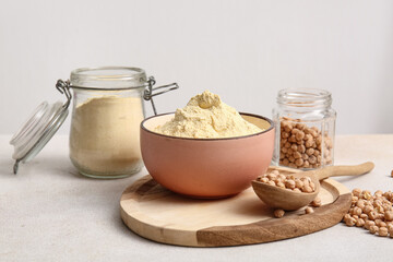Bowl of chickpea flour and wooden spoon with beans on white background
