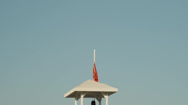 Lifeguard on a Tower by the Sea Raising a Red Flag, Prohibiting Entry into the Water.