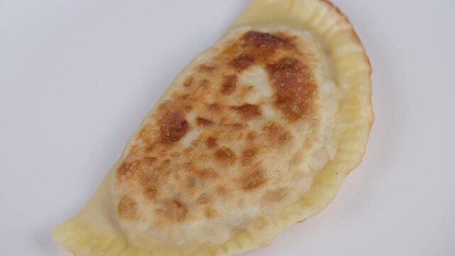Fried cheburek on plain dish. Golden brown cheburek with minced filling closeup. Closeup of golden fried cheburek with textured crust and flavorful minced meat filling