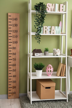 Interior of modern children's room with wooden stadiometer and shelving unit