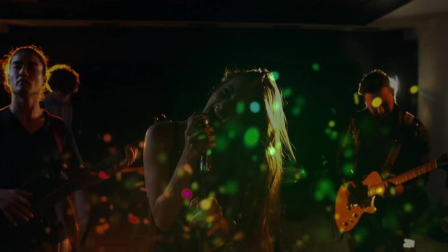 Singer flipping hair and causing colored light particles while band rehearsing music