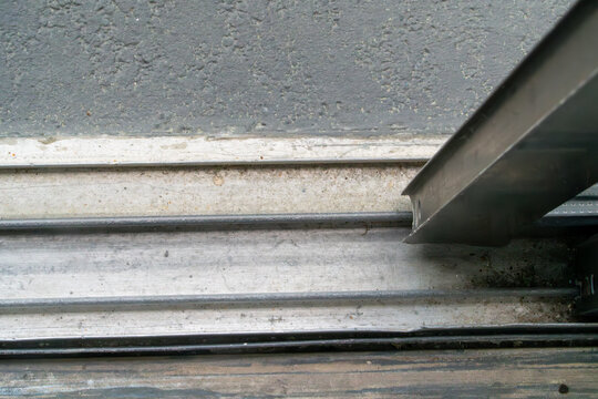 Close-up of a weathered, dirty sliding door or gate track mechanism on rough concrete, featuring worn metal rails and an industrial aesthetic.