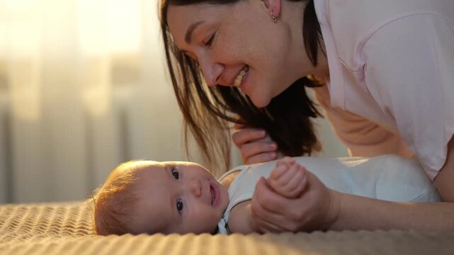 Mother And Baby Play. Joyful Mother Interacts With Infant. Mother And Child Share Laughter During Daytime Nursery Fun. Mother Amusing Her Baby With Peekaboo On Bed During Warm Sunlight