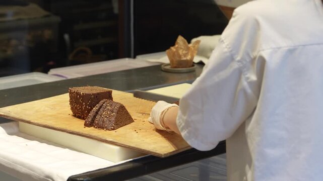 Professional Baker Slicing Dark Rye Bread with Seeds. Chef slicing a triangular loaf of dark coriander rye bread on a wooden board. Professional kitchen setting for bakery, restaurant