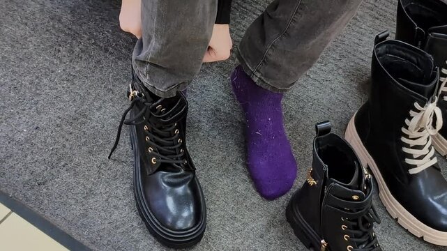 Putting on black boots with purple socks in a store at a mall
