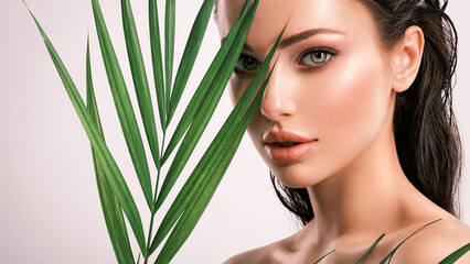 Fototapeta premium Young beautiful woman with green leaves near face. Skin care beauty treatments concept. Closeup girl's face with green leave.