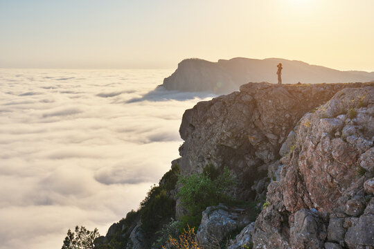 Landscape of High Rock Cliff Above Sea of Clouds at Golden Hour Sunset with Girl Silhouette Concept