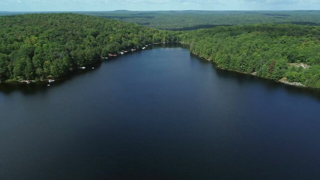 Flying over Buckskin Lake on an overcast, late summer afternoon. Aerial above lakeside cottages along side expansive wilderness of crown land in Tory Hill, Halliburton Highlands East, Ontario, Canada.