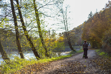 Obraz premium Woman pushing stroller on autumn forest path by pond