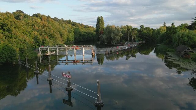 Serene river scene with a lock gate, lush trees, and reflections in the water. A 'Danger' sign is visible.