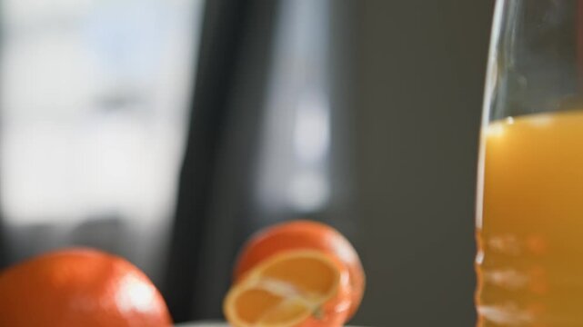 Macro view: man's hand lifts glass of orange juice to drink at breakfast table. Palm tree in soft bokeh behind, bright sunlight from window illuminates juice and creates fresh energizing morning vibe