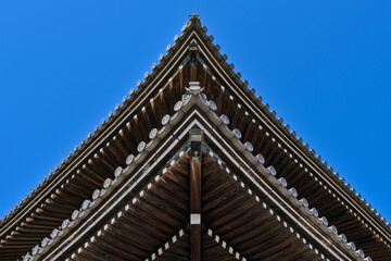 Symmetrical low angle view of a traditional Japanese wooden temple roof against a clear blue sky © naoto_film