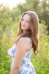 Naklejka premium Sunlit Senior Portrait of Girl in Floral Dress Warm Golden Hour Glow.