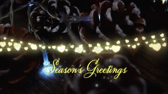 Animation of text, season's greetings, in yellow, over string lights and pine cone decorations