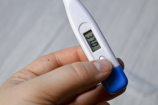Hand holding digital thermometer showing 37.0&deg;C, close up. Body temperature measurement, fever check, healthcare, illness, home diagnosis and medical concept.