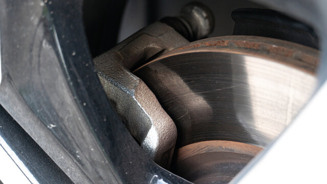 Detailed close up of a vehicle's disc brake system. Featuring a worn metal rotor and brake caliper assembly. Highlights the mechanical components behind the wheel.