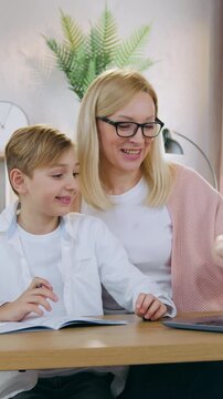 Likable surprised 12-aged boy sitting in front of computer together with his adorable positive loving blond mom and watching at results of online test which he did with mother ,home education concept