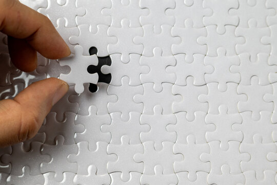 Hand placing puzzle piece into white puzzle