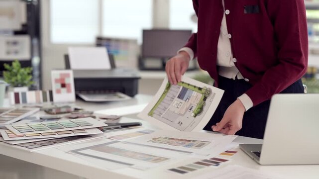 Adult Asian architect designer reviewing architectural blueprint plans modern office creating project interior design selecting color swatches professional workspace