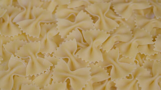 Raw pasta closeup. Dried bowtie pasta detailed view. Uncooked farfalle with shadowed studio lighting. Closeup of dry bowshaped pasta with filling details and warm tones