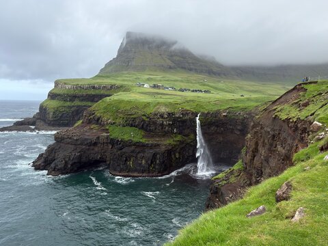 Green landscapes of the Faroe Islands. Incredible view of Mulafossur waterfall flowing into the Atlantic Ocean. Gasadalur village, Vagar Island.