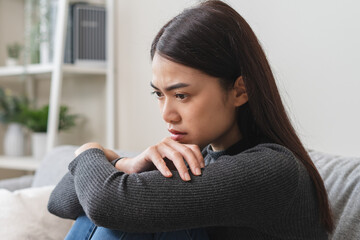 Unhappy anxiety young Asian woman covering her face with pillow on the cough in the living room at...