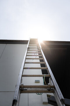 An aluminium ladder is leaning on the house roof, using for climbing ascent up to roof top for building activity susch as installing the solar cell. Close-up and selective focus at ladder's part.
