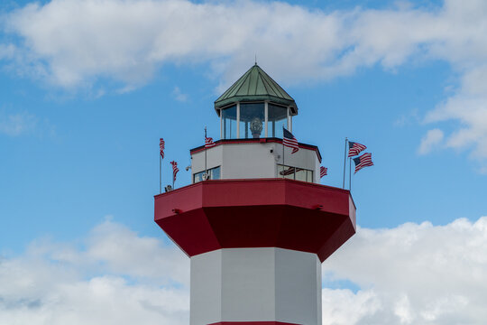 Iconic Harbour Town Lighthouse in Hilton Head Island, South Carolina, USA, adorned with American flags against a vibrant blue sky, a striking red and white beacon with a distinctive green cap.