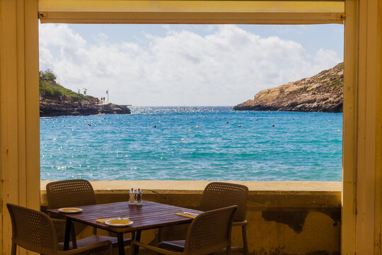 Seaside Restaurant Table With Chairs Overlooking Turquoise Mediterranean Bay Through Open Window