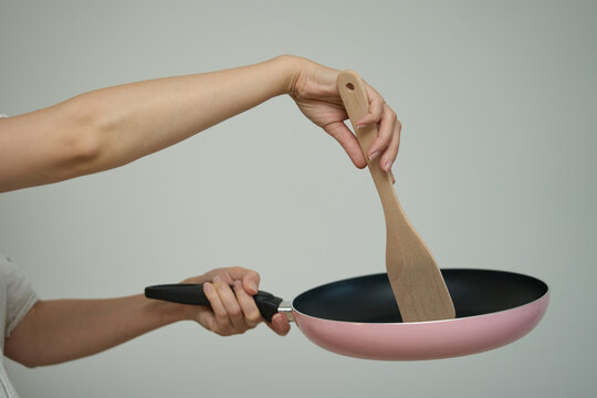Frying pan in human hands, Cooking concept. Hand holds a pink frying pan by the handle, showing the metallic textured bottom surface.