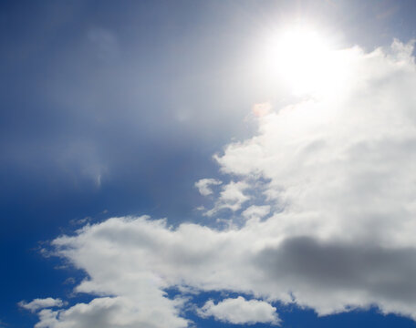 Bright light of the sun on a dark blue sky among the clouds. Dramatic view of the sun.