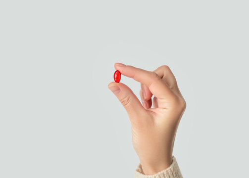 Hand holding a red pill capsule