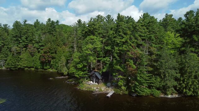 Flying over Buckskin Lake, in a circular motion around an old creepy hunting lodge on a summer afternoon. Aerial over crown land wilderness, in Tory Hill, Highlands East, Ontario, Canada.