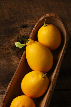 Lemons Still Life. Vertical overhead shot of four ripe lemons in a long narrow wooden bowl.