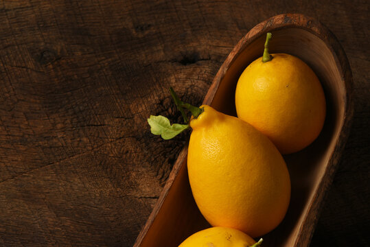 Closeup of three ripe lemons in a long narrow wooden bowl