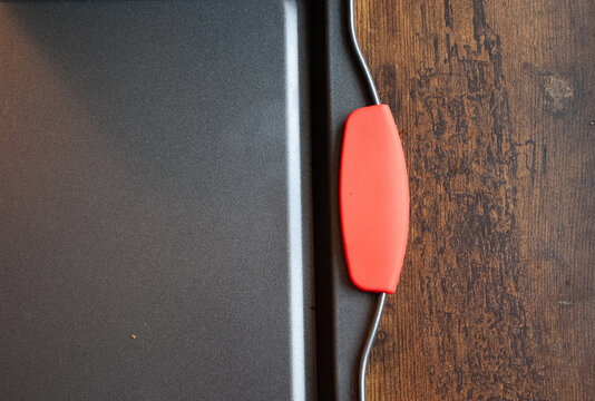 Contemporary dark grey non-stick baking pan with a vibrant red silicone handle resting on a warm, textured wooden background, highlighting modern kitchenware design and materials.