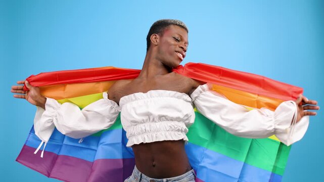Proud non binary person smiling and dancing covered with a rainbow lgbt flag. Studio shot symbolizing freedom, love, and equality