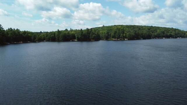 Flying over Buckskin Lake on a late summer afternoon towards lakeside cottages. Low aerial above the water among the crown land wilderness located in Tory Hill, Highlands East, Ontario, Canada.