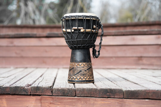 Hand-carved wooden djembe drum with ethnic patterns and rope tuning on a deck.  Traditional African djembe drum on a wooden stage outdoors.