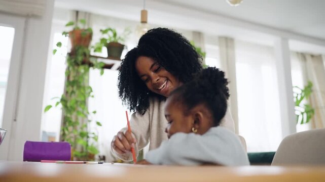 Cheerful mother enjoying a creative afternoon with her little daughter. The family is sitting at a wooden table, drawing with crayons