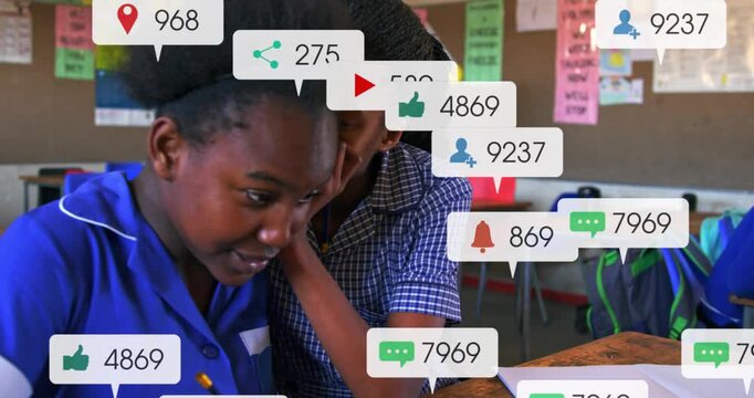 Two girls writing at wooden desk in classroom, notification badges appearing and distracting work