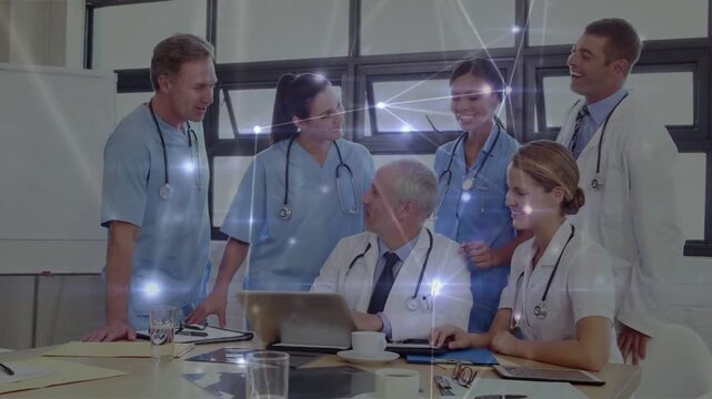 Senior MD using laptop; female MD pointing at screen, causing network overlay, medical team smiling