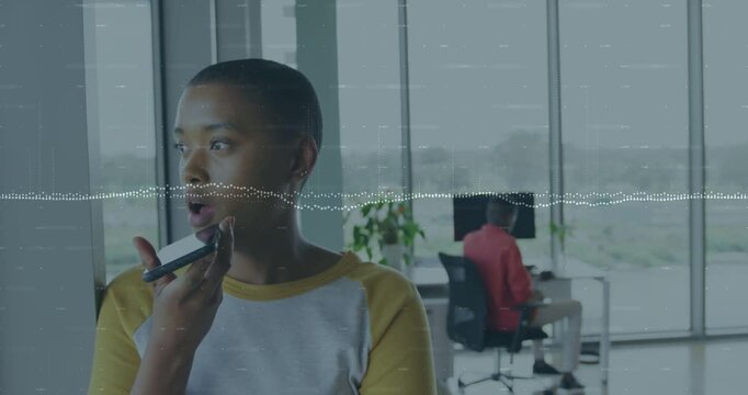Woman speaking into cell in office by window recording update, causing waveform while peer exiting