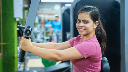 Fototapeta premium Indian Woman Performing Butterfly Exercise on Pec Deck Machine During Chest Workout in Modern Gym