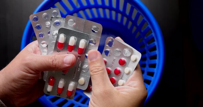 Person discarding various pill blisters in a blue bin for medical malpractice concepts and pharmaceutical treatment interruptions.