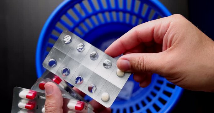 Hands throwing used medication blisters into a blue trash can to represent medical malpractice and dangerous pharmaceutical errors.