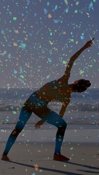 Vertical video: Woman shifting into side-bend on beach for yoga, confetti overlay partly obscuring