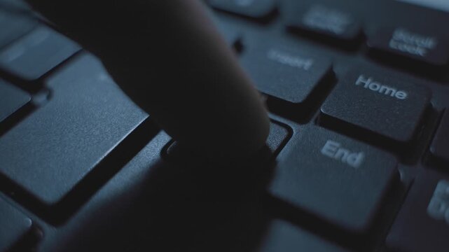 Finger pressing on delete key button on computer keyboard in dark office. Extreme close up. Person deleting information text or digital file. Hacker or programmer coding software clearing data